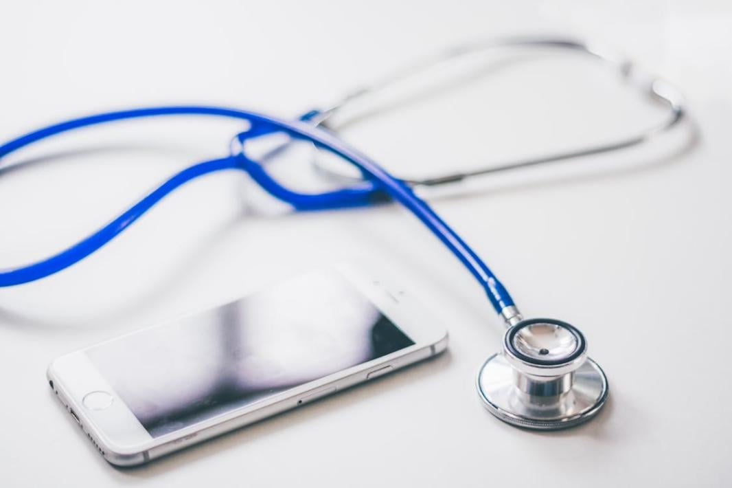 A silver smartphone lies next to a blue and silver stethoscope on a white surface, representing the intersection of technology and medicine.