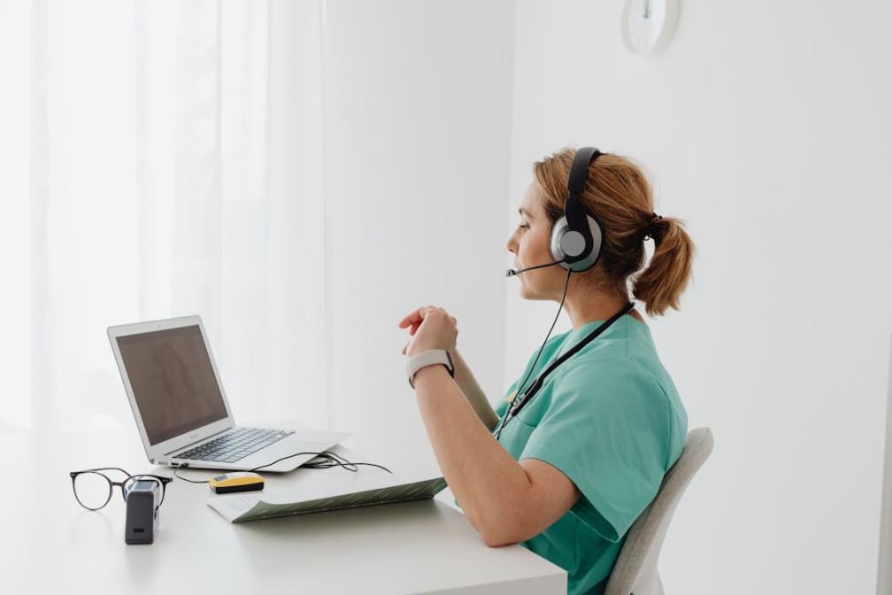 A female doctor with a stethoscope while looking at a laptop screen during a video call.