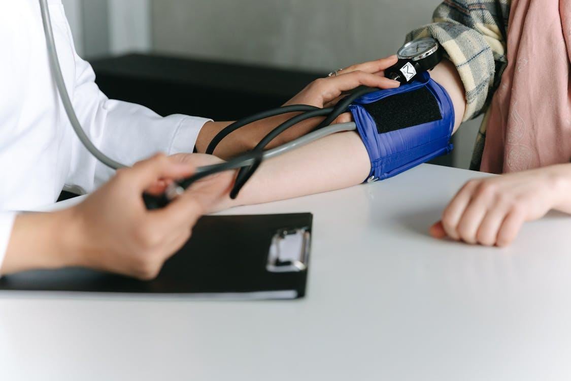 A healthcare professional uses a blood pressure cuff and sphygmomanometer on a patient's arm to take a clinical reading.