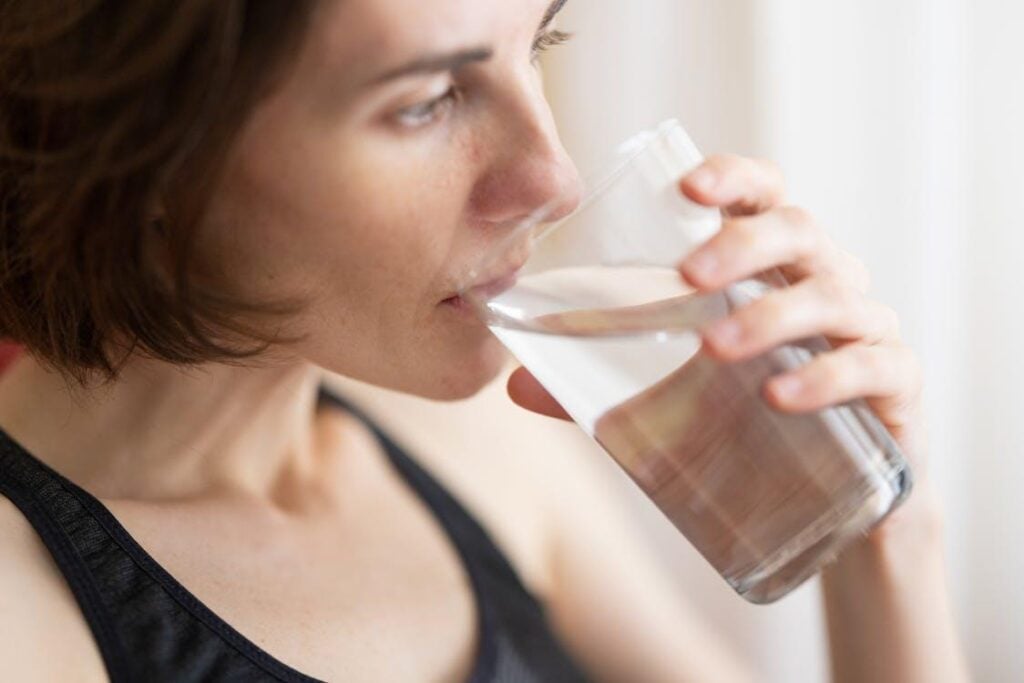 A woman drinks water from a clear glass.