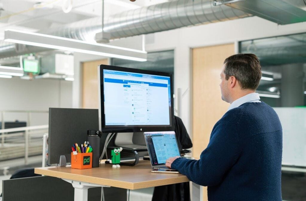 A man uses a laptop at a raised standing desk.