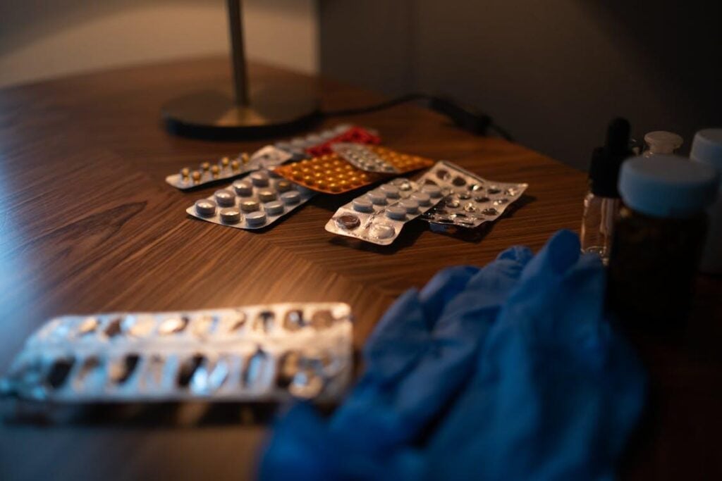A selection of medication capsules and tablets laid out on a surface next to blue medical gloves.