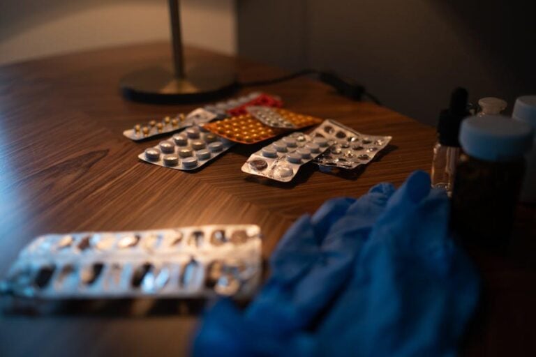 A selection of medication capsules and tablets laid out on a surface next to blue medical gloves.