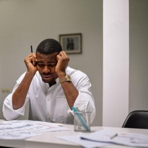 A man sits at a cluttered office desk, looking extremely stressed and frustrated.