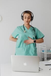 A female doctor conducts a video call on a laptop, using her hands to demonstrate the placement.