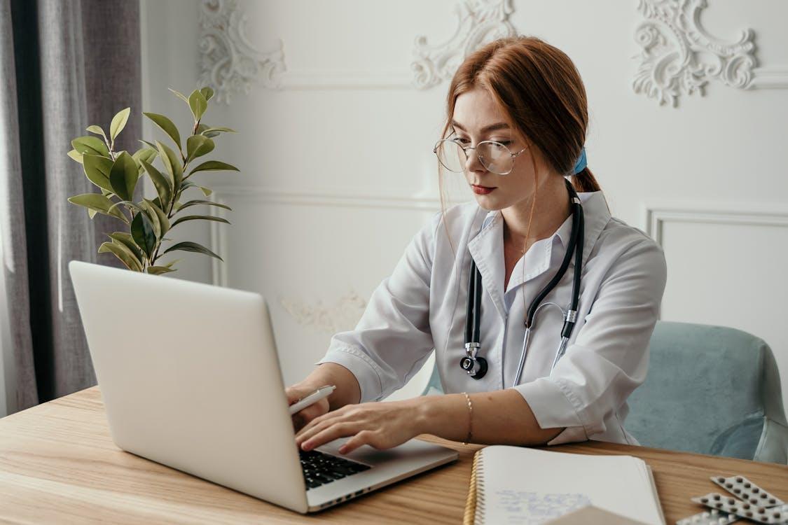 A doctor types on a laptop.
