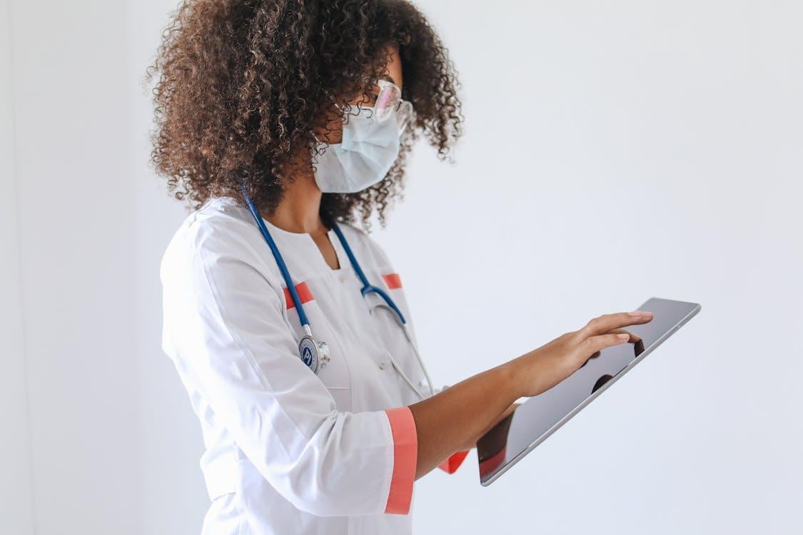 A medical professional wearing a surgical mask uses a digital tablet in a professional healthcare setting.