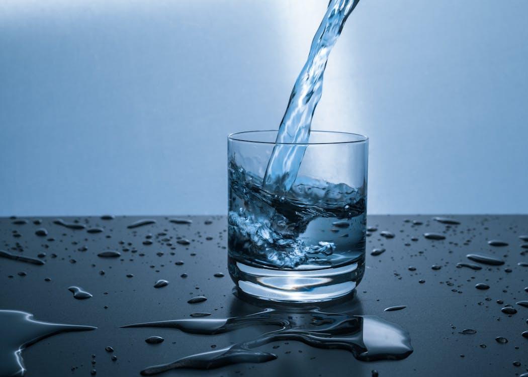 Fresh, clear water being poured into a transparent glass.
