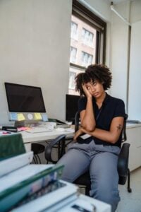 A woman sits slumped in her office chair, looking exhausted and drained while at her desk.