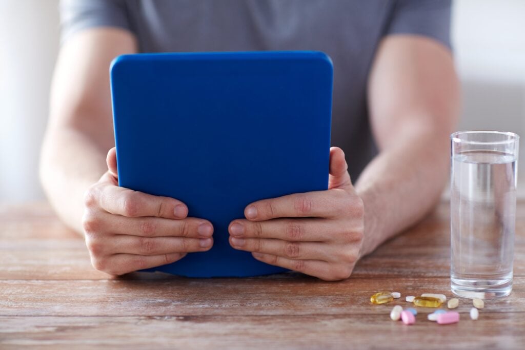 Person holding a tablet during a virtual urgent care consultation with medication and water nearby
