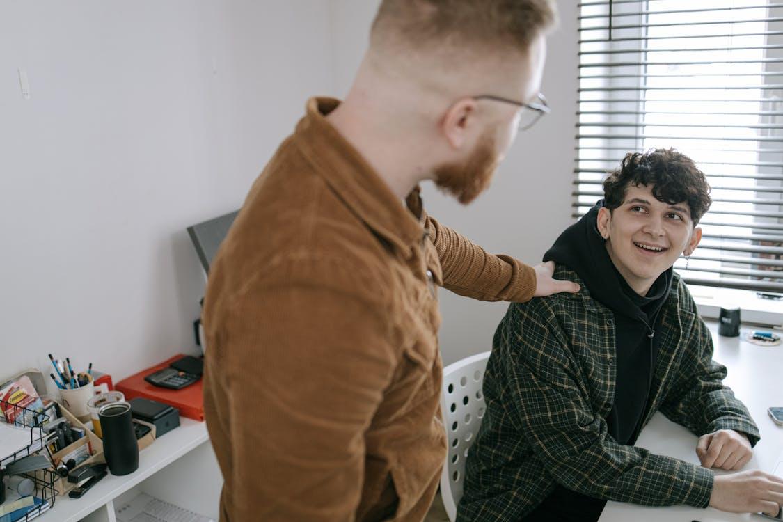 Two colleagues in a modern office setting are engaged in a supportive conversation.