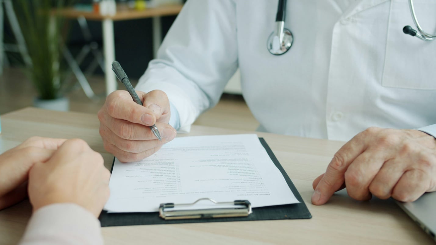 A doctor writing on a clipboard with a pen