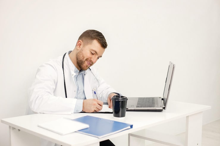 Doctor using a laptop to prepare medical documentation during a virtual patient consultation.