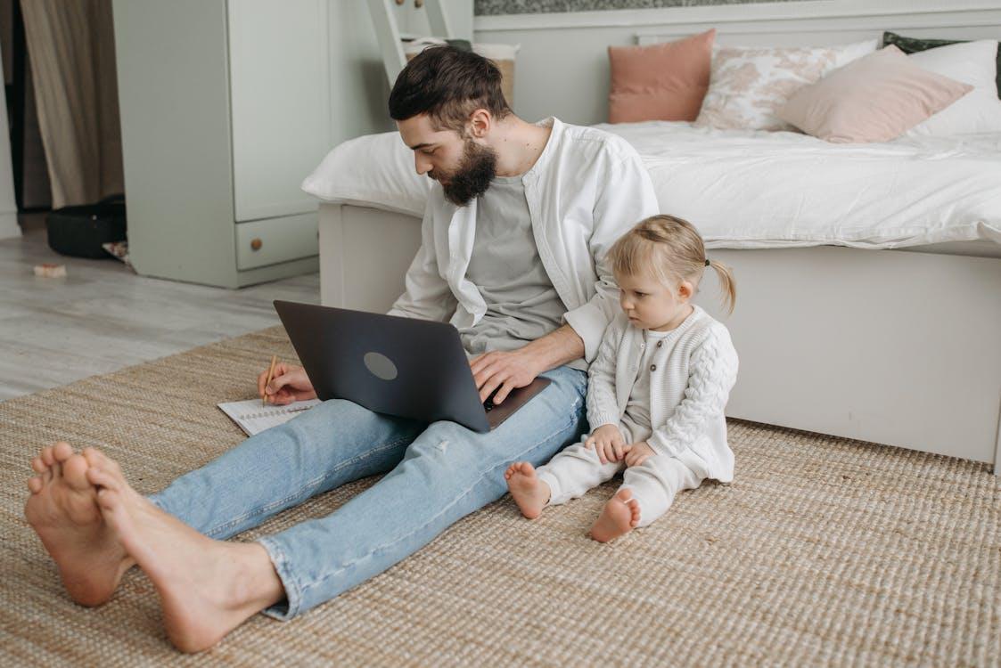 A person working on a laptop in their bedroom with a child next to them
