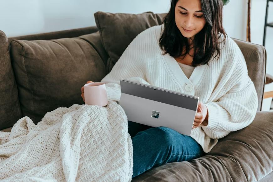 A person holding a laptop and a mug while sitting on the couch