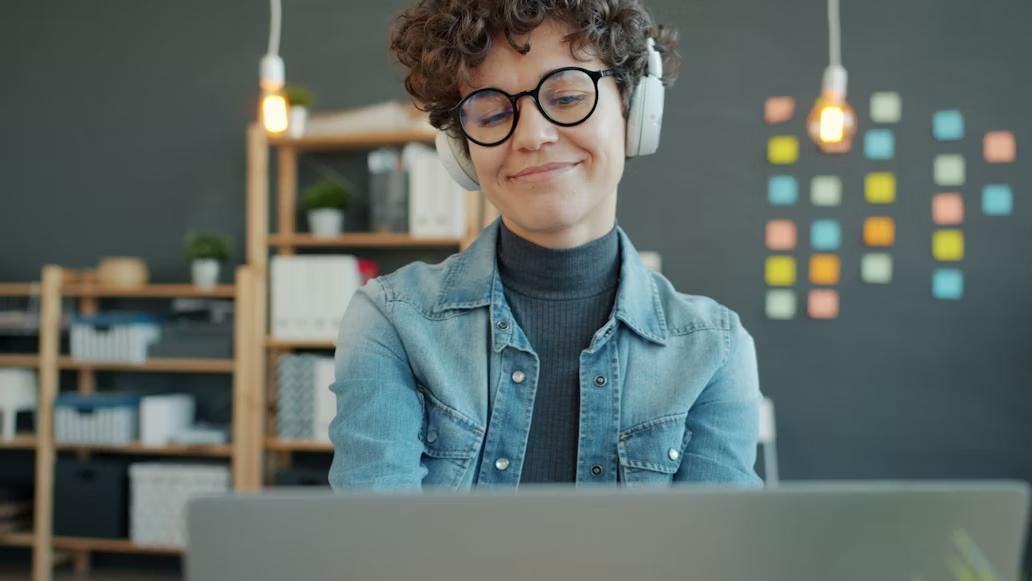 A person wearing headphones and smiling when looking at the laptop
