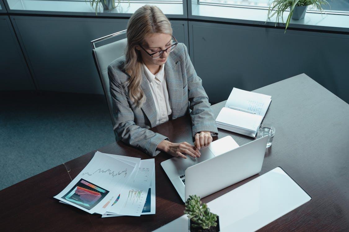 An executive typing on a laptop next to papers on their desk